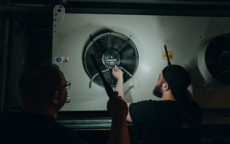 Mitarbeiter kontrollieren Lüftungstechnik mit Taschenlampe und Werkzeug
